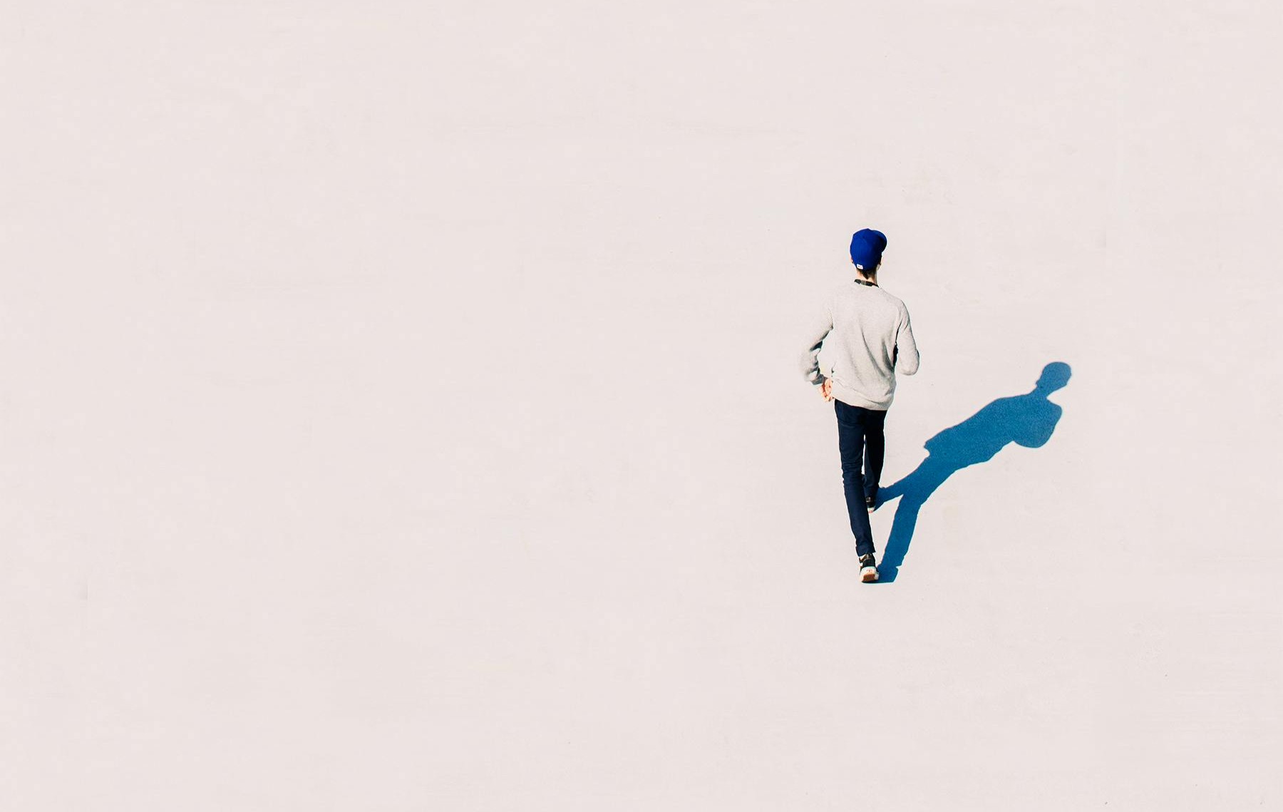 A person walking alone on a wide, open white surface, casting a long blue shadow — symbolizing the journey from feeling invisible to becoming seen and taking up space.
