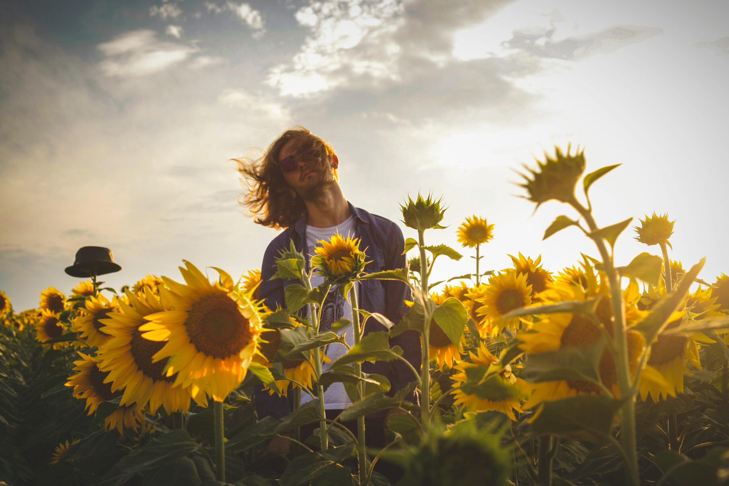 A person standing in a sunflower field at sunset, hair blowing in the breeze, with the title ‘This Is Your Reminder to Breathe.’
