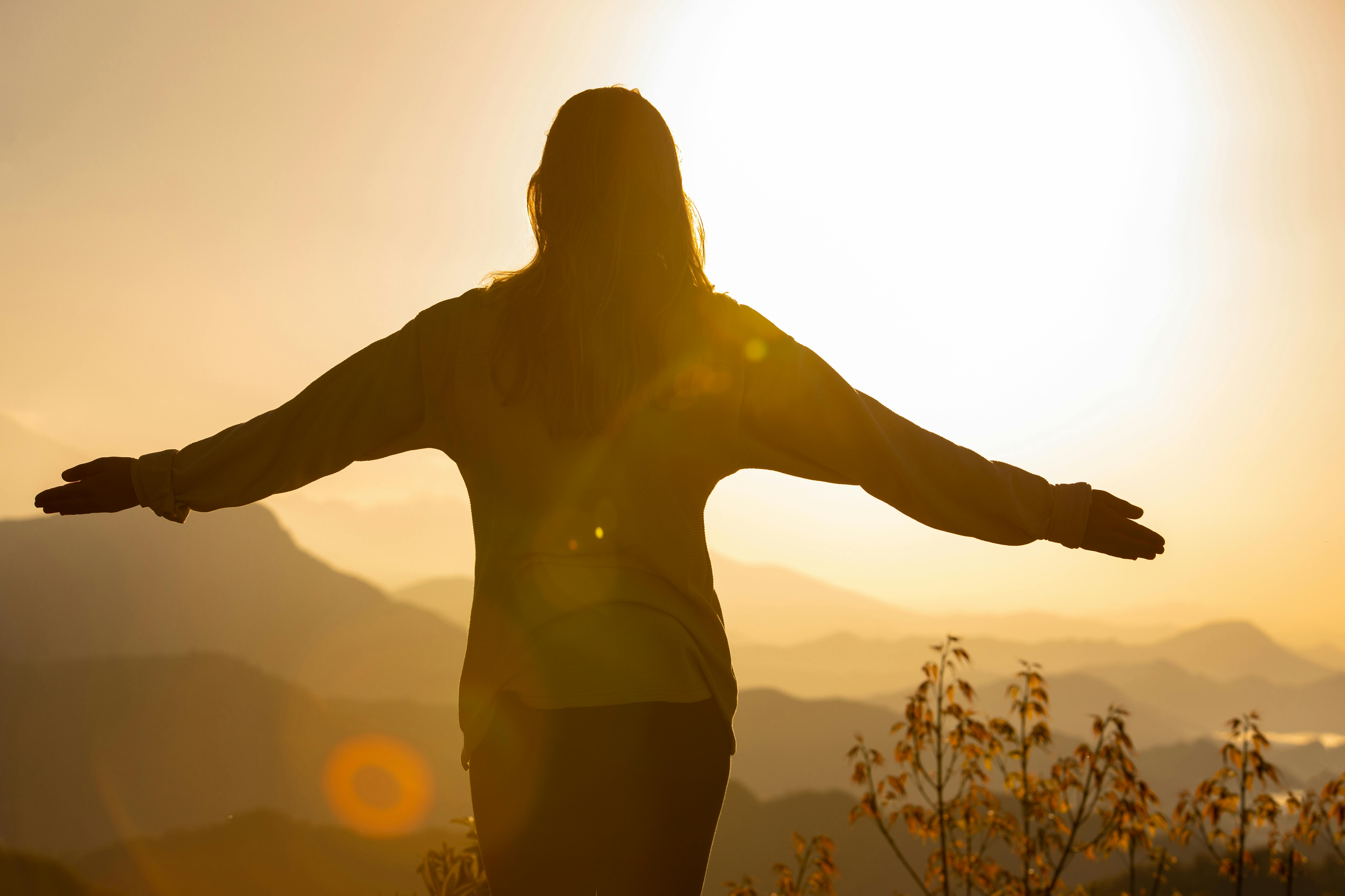 Silhouette of a woman standing with arms outstretched at sunrise over mountains, symbolizing healing, unity, and inner wholeness at Joy Spring Mental Health.