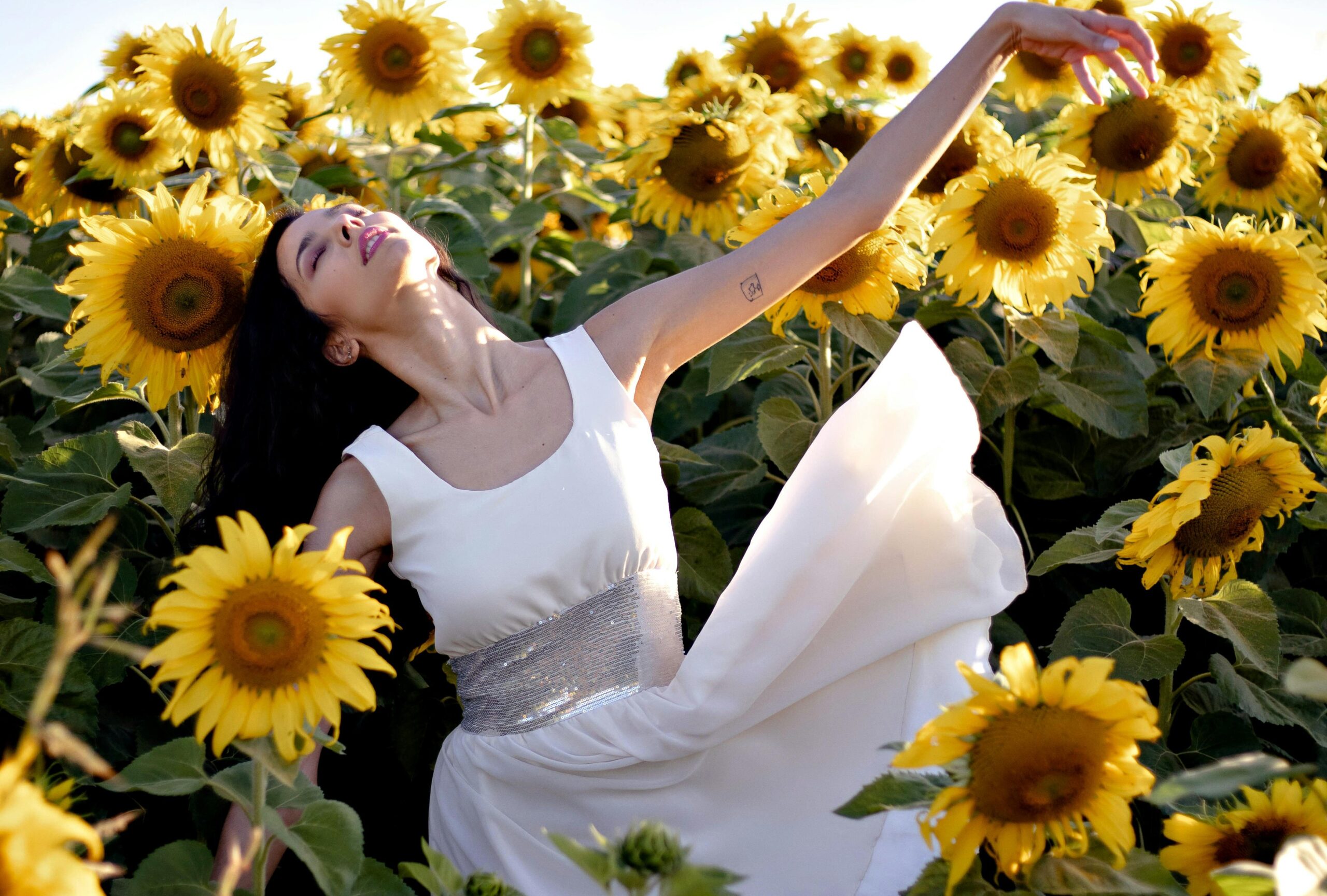 Woman in a flowing white dress gracefully dancing among vibrant sunflowers, expressing freedom and joy — Emotions in Motion.