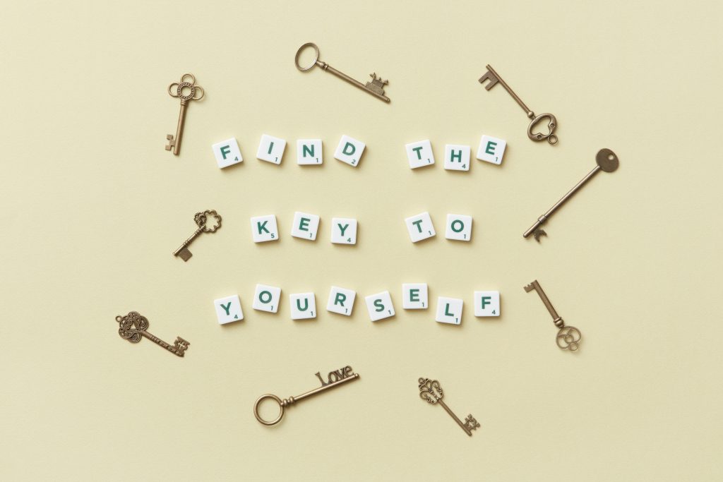 Flat lay of vintage keys arranged around Scrabble tiles spelling “Find the key to yourself” on a beige background, symbolizing self-discovery and personal growth.