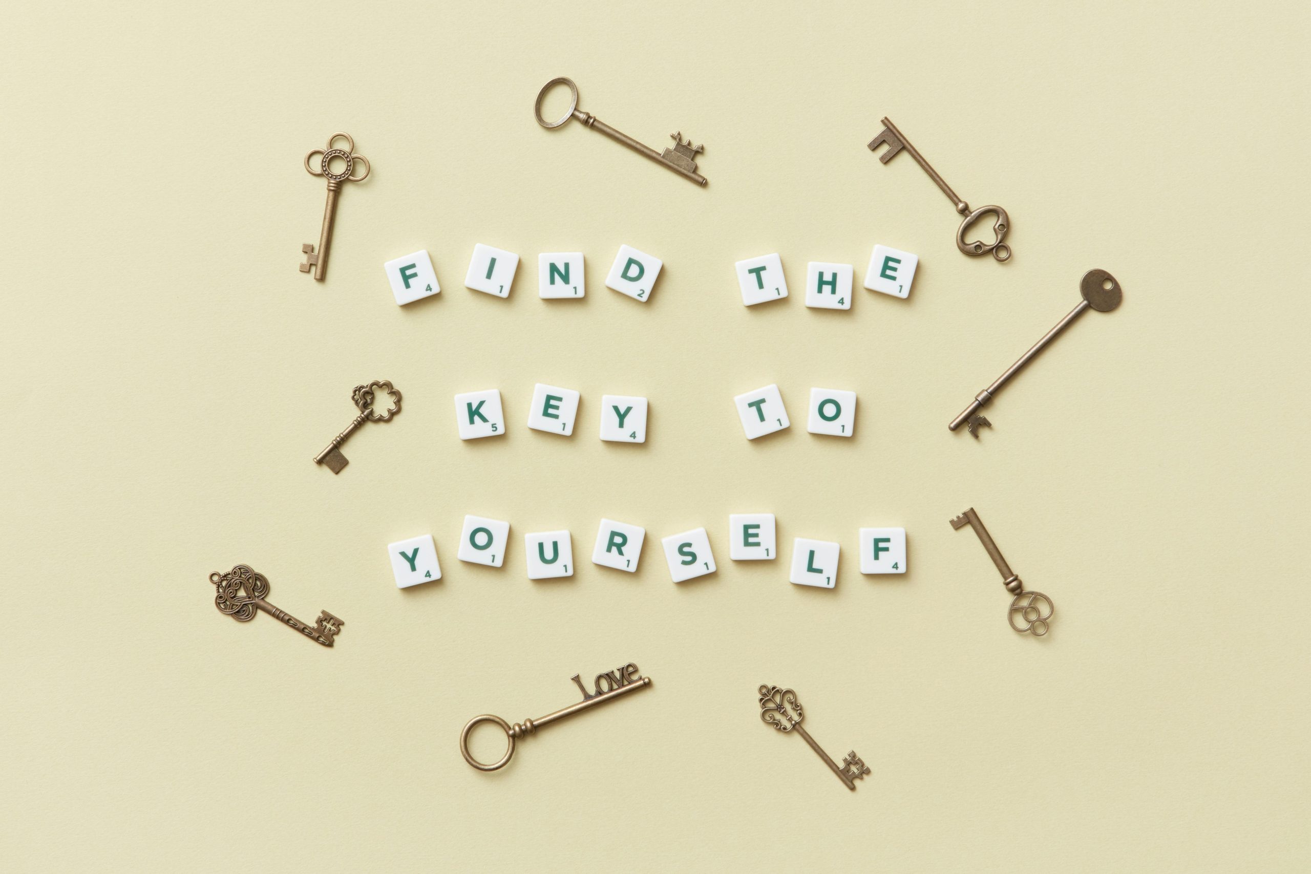 Flat lay of vintage keys arranged around Scrabble tiles spelling “Find the key to yourself” on a beige background, symbolizing self-discovery and personal growth.