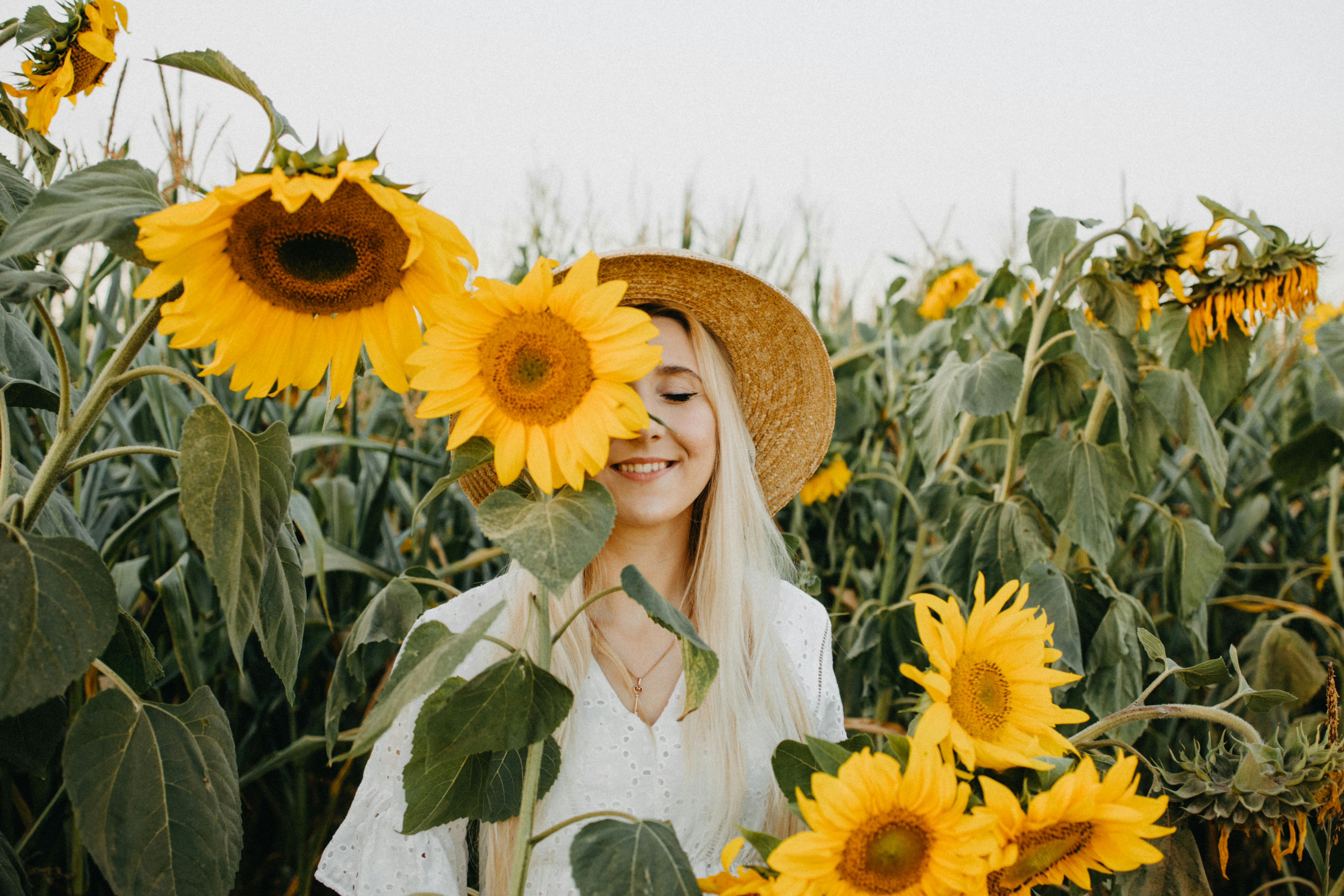 A young woman in a straw hat smiles among tall sunflowers, symbolizing “The Myth of Pain-Free Living” by embracing joy alongside life’s struggles.