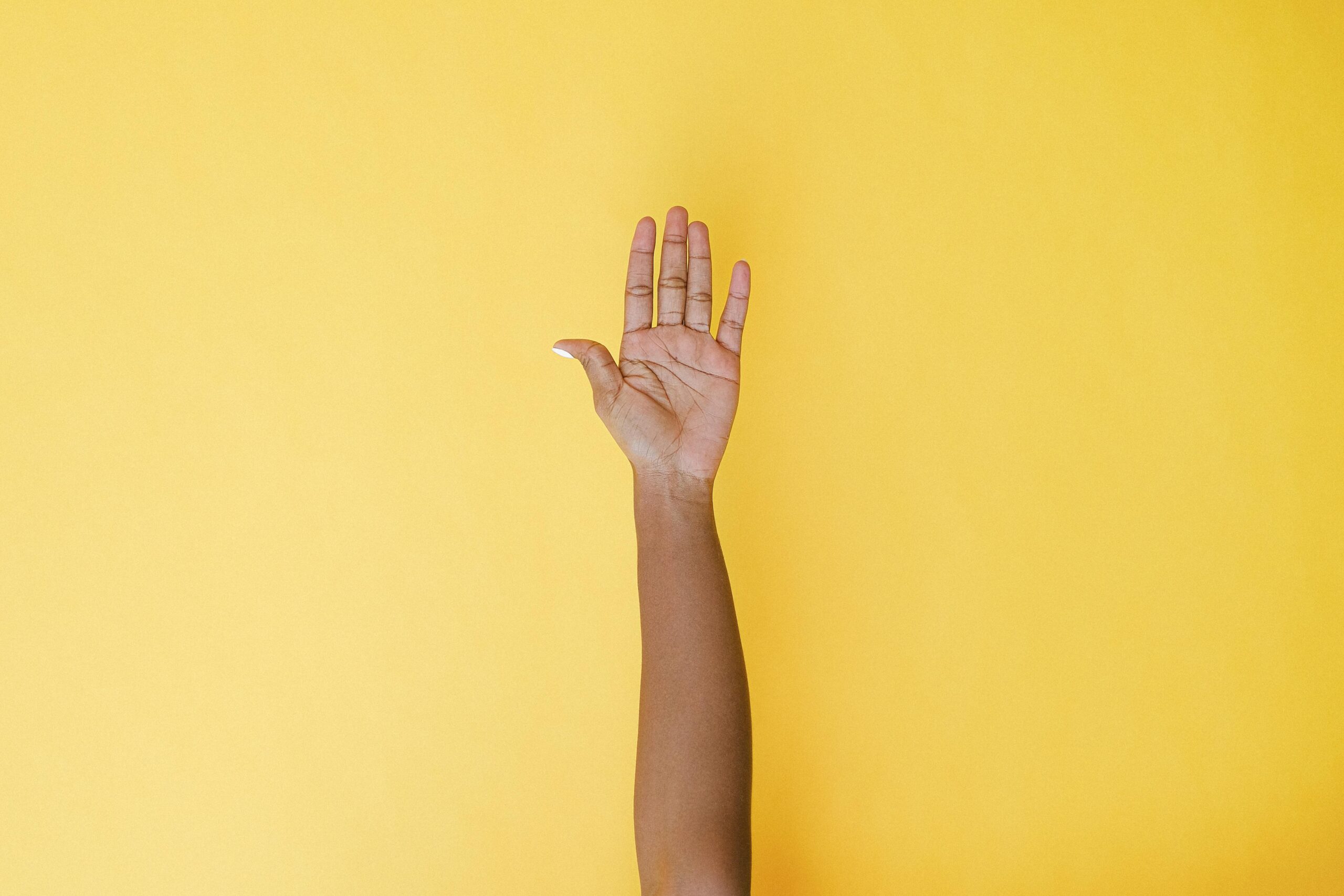 A raised hand against a bright yellow background, symbolizing the quiet courage of reaching out and asking for help.