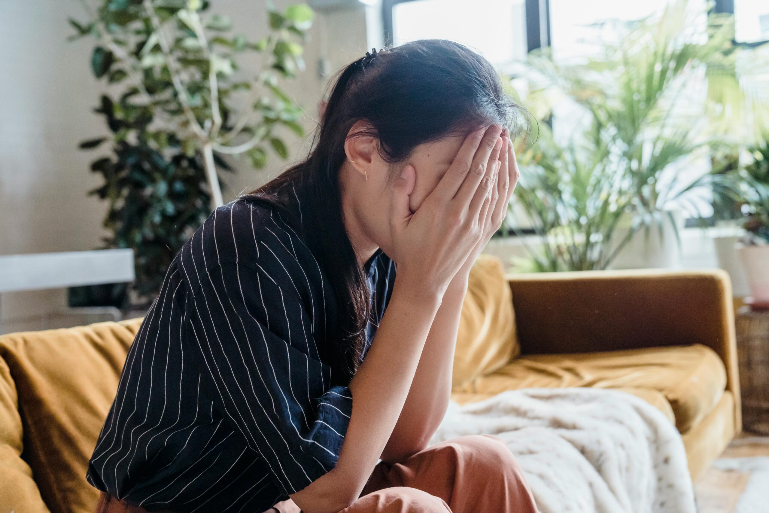 Woman sitting on a sofa with her face in her hands, expressing grief and sadness, symbolizing the emotional weight of loss and the journey of healing.