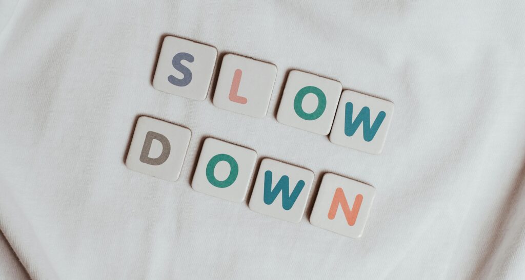 Letter tiles arranged on a soft white fabric spelling the words ‘SLOW DOWN,’ symbolizing mindfulness, rest, and taking time for self-care