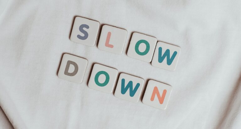 Letter tiles arranged on a soft white fabric spelling the words ‘SLOW DOWN,’ symbolizing mindfulness, rest, and taking time for self-care