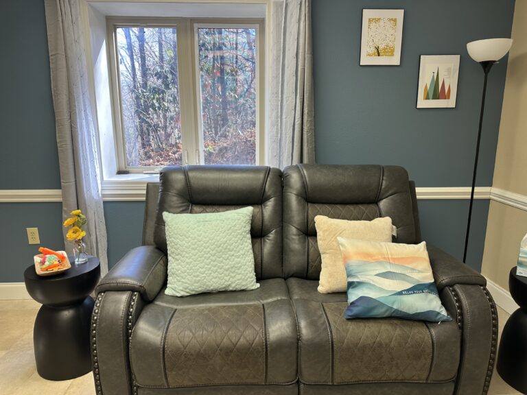 A cozy therapy room with a dark leather loveseat and teal accent wall at Joy Spring Mental Health in Hendersonville, NC.