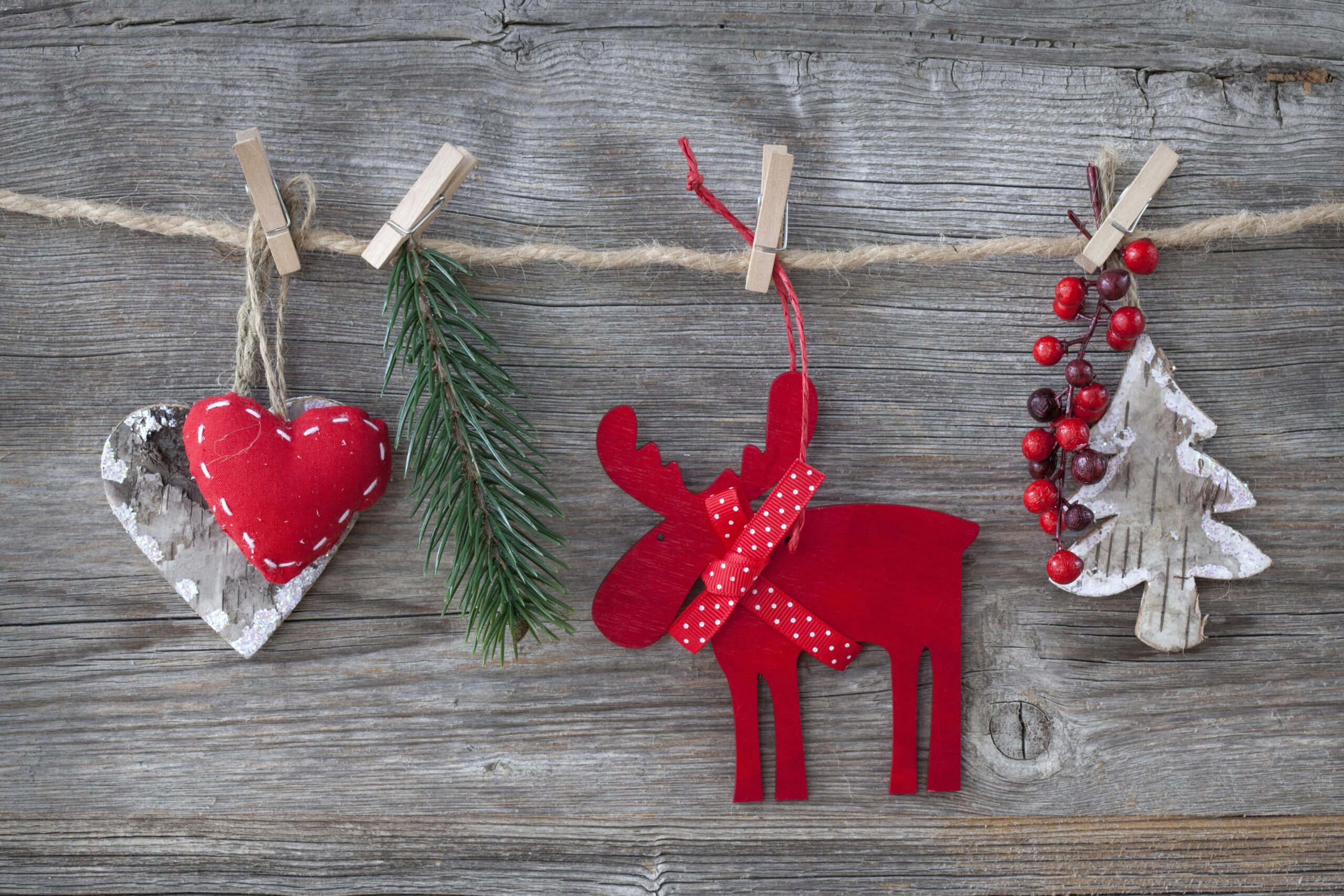 Rustic holiday decorations clipped to a twine line on a wooden background, including a red heart, pine sprig, red reindeer ornament, and winter greenery, symbolizing warmth, healing, and seasonal care.