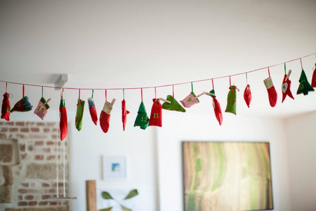 A string of small red and green fabric pockets numbered like an advent calendar hangs across a bright, cozy room, suggesting simple, calming moments during the holiday season.