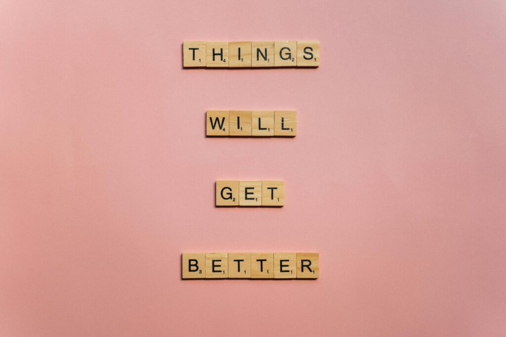 Motivational message spelled out with wooden letter tiles on a pastel pink background reading, ‘Things will get better.