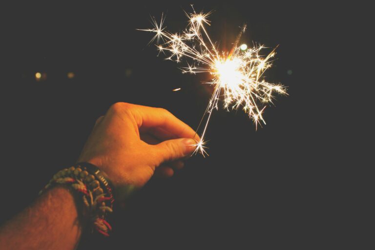 A hand holding a lit sparkler against a dark background, with bright sparks radiating outward, symbolizing a quiet, hopeful start to the new year.