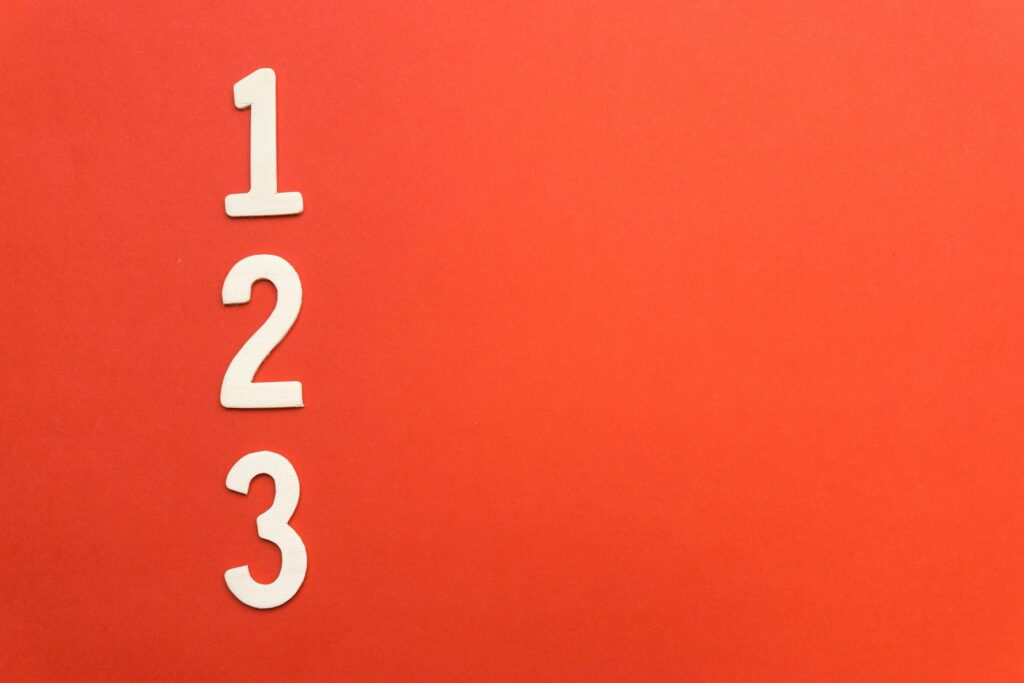 Numbers 1 2 3 on red background symbolizing doing one task at a time to reduce overwhelm and support mental health.
