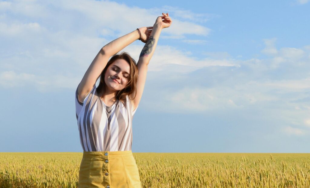 Woman stretching in a sunny field during spring, representing better movement and mental wellness.