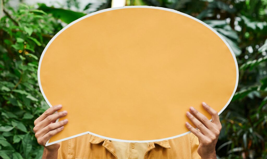 Person holding a blank orange speech bubble sign in a natural setting, representing expressing needs and communication in mental health support