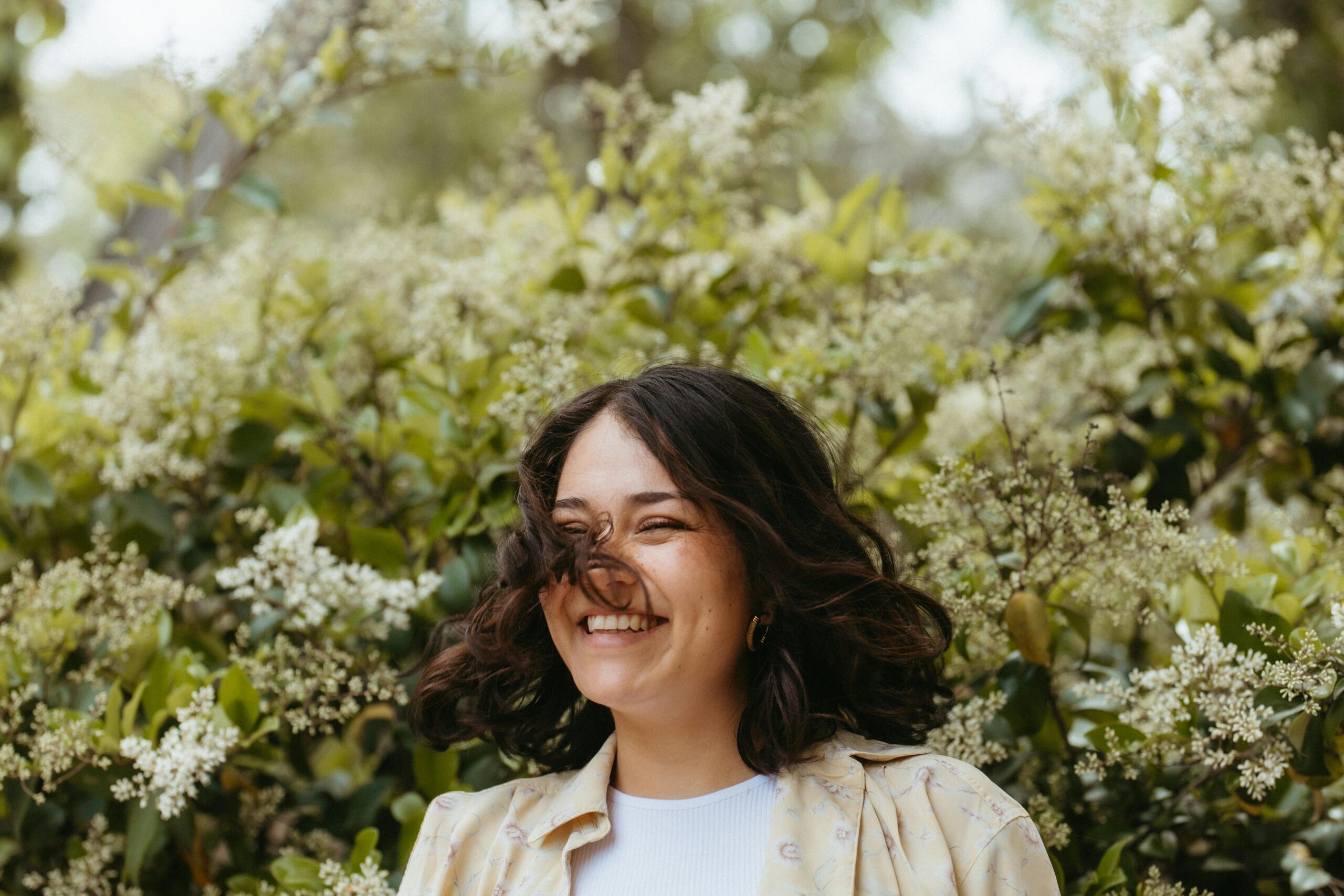 Smiling woman outdoors surrounded by spring blossoms, representing emotional wellness and coping with seasonal change stress.