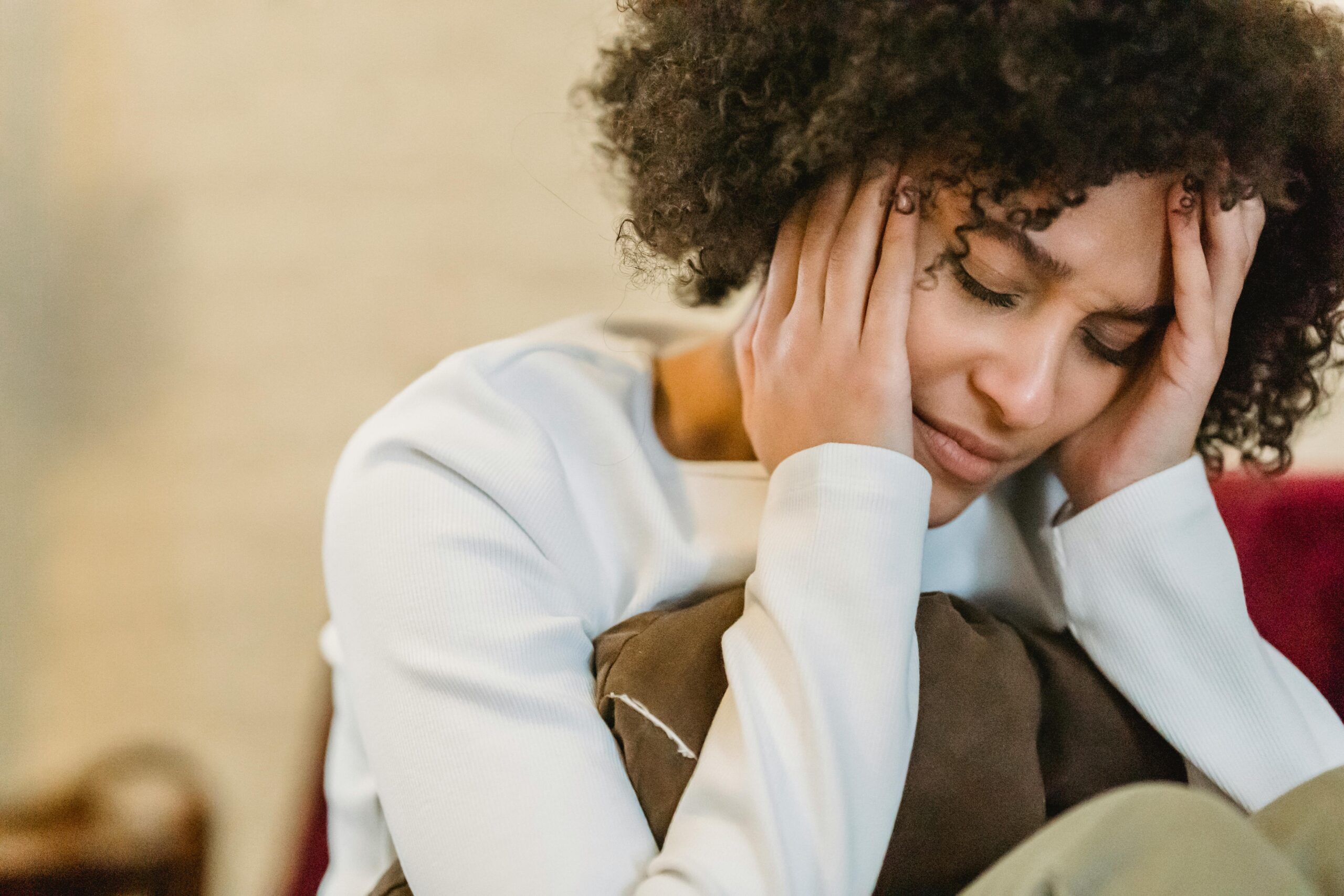 Woman sitting on a couch holding her head with eyes closed, appearing overwhelmed or anxious, illustrating the need for grounding techniques and mental health support.
