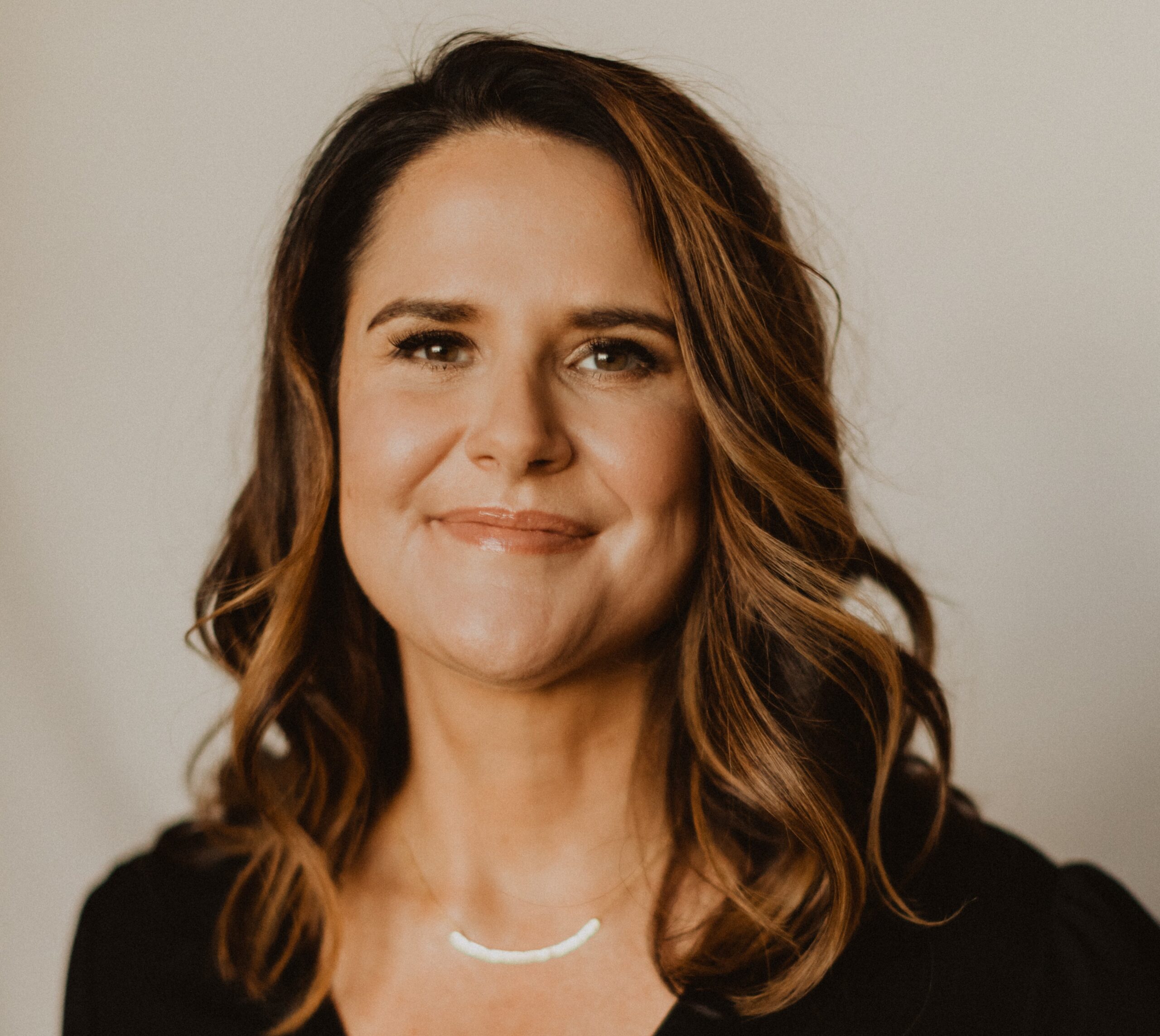 Brandy Colvin, Joy Spring Mental Health – Professional headshot of Brandy Colvin smiling gently at the camera. She has shoulder-length wavy brown hair with subtle highlights, wears a black top and a delicate silver necklace, and is photographed against a soft neutral background.